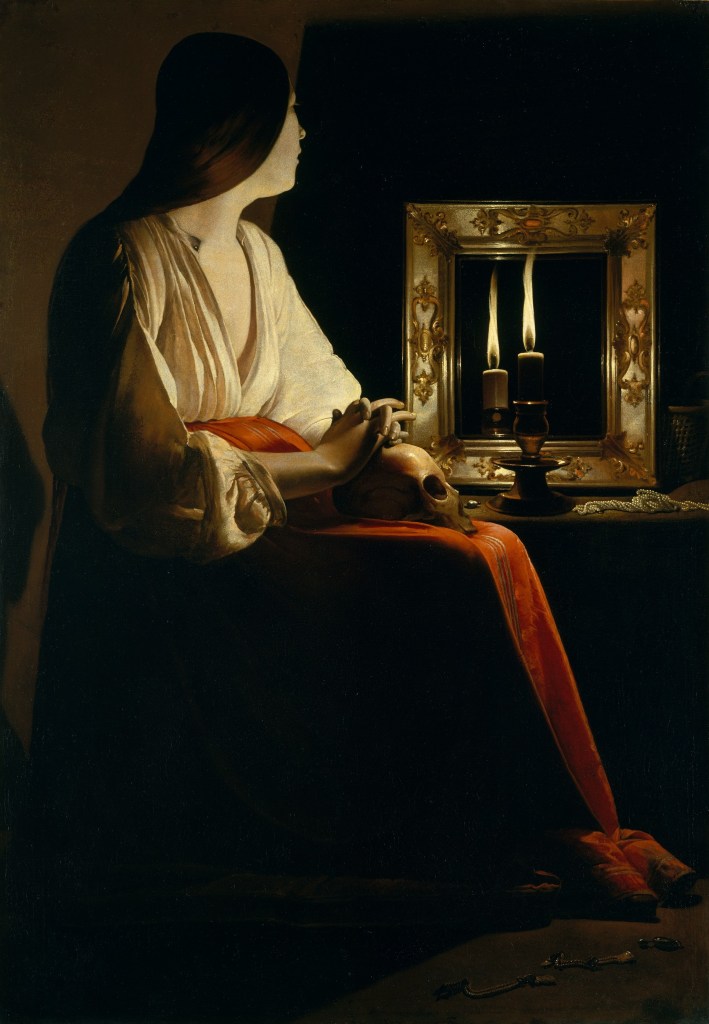 Rappresentazione di Maria Maddalena in una posa contemplativa, con lunghi capelli scuri e vestiti chiari. Tiene un teschio tra le mani e guarda verso una cornice con candele accese, simboleggiando la ricerca spirituale e l'introspezione.